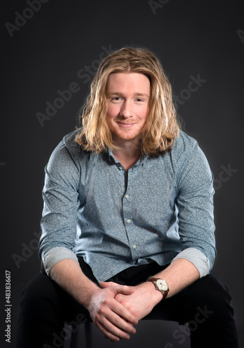 Handsome blonde long haired male model arms sitting isolated on black background