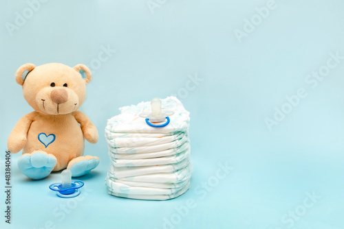 Stack of diapers with cute teddy bear toy on table. set for infant newborn boy girl for baby shower present gift on blue background. Healthcare medical, hygiene concept