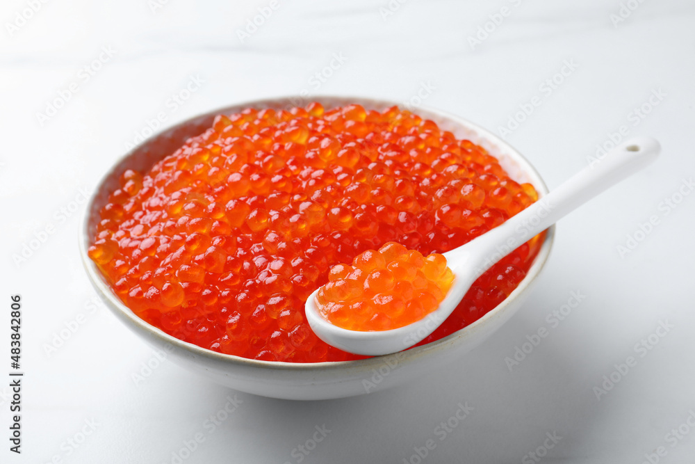 Bowl and spoon with delicious red caviar on white table Bowl and spoon with delicious red caviar on white table