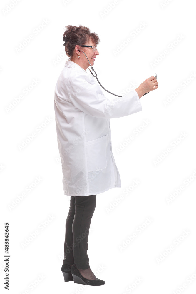 Side view of serious mature woman doctor in a white coat listens with a stethoscope to an invisible object posing on a white background Side view of serious mature woman doctor in a white coat listens with a stethoscope to an invisible object posing on a white background