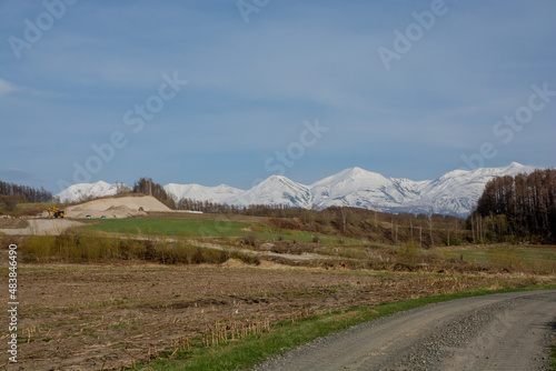 春の農村のジャリ道と雪山 十勝岳連峰 