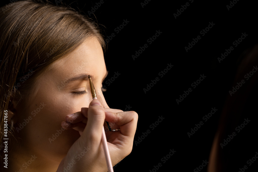 Makeup artist doing a eyebrows makeup on a beautiful woman face. Hand of make-up master is painting eyebrow of young beauty model girl. Make up in process. Makeup artist doing a eyebrows makeup on a beautiful woman face. Hand of make-up master is painting eyebrow of young beauty model girl. Make up in process.