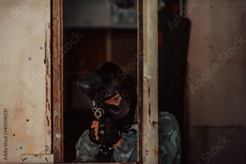 Photo of paintball player in goggle mask and camouflage aiming by paintball gun. Selective focus