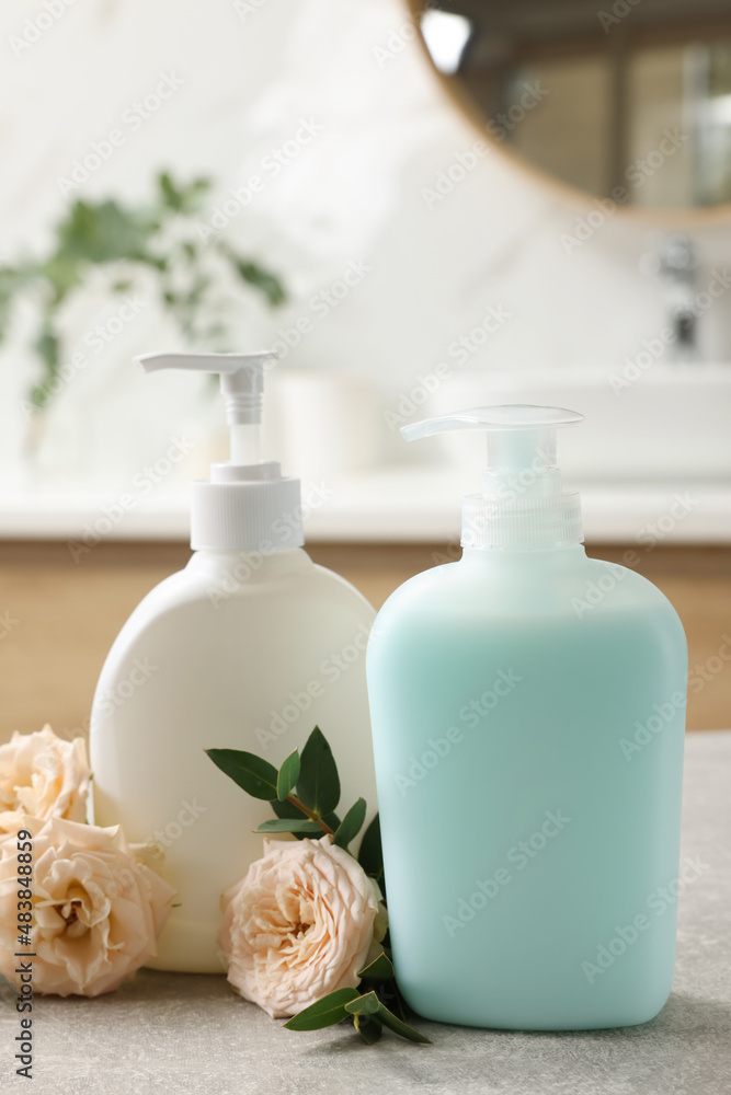 Dispensers of liquid soap and roses on light grey table in bathroom