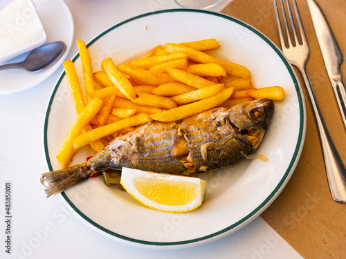 Delicious baked salema porgy with side dish of fried potatoes and fresh lemon photo