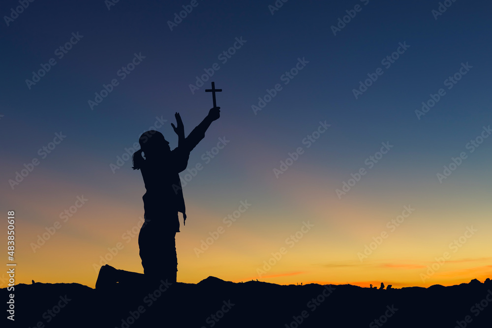 Silhouette woman praying and holding Christian cross for worshipping God sunset sky background. Christian, Christianity, Religion copy space background