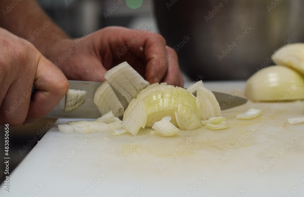 Restaurant kitchen employee cutting onions with knife closeup