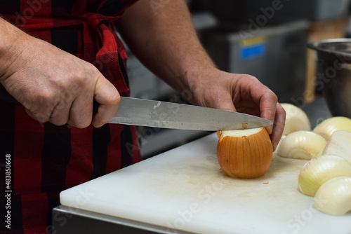 Restaurant kitchen employee cutting onions with knife