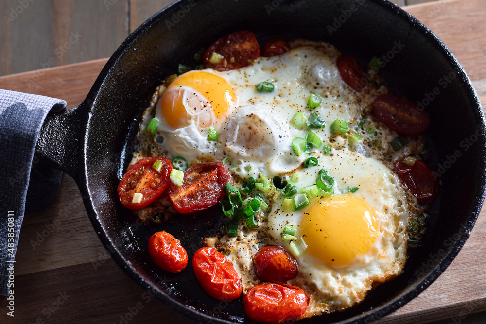 Top down view of breakfast eggs with tomatoes and green onions in cast iron pan Top down view of breakfast eggs with tomatoes and green onions in cast iron pan
