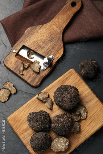 Wooden shaver with whole and sliced truffles on black table, flat lay photo