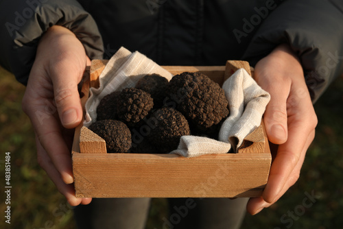 Woman holding wooden crate with truffles outdoors, closeup