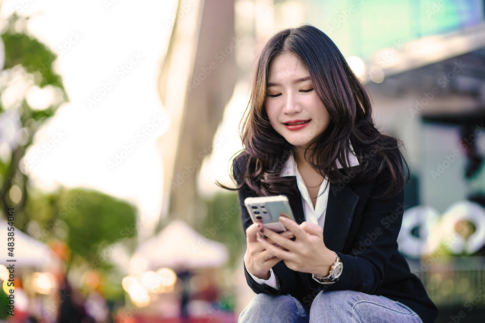Asian woman happily sitting on the sidewalk and use the phone to chat with friends via social media.