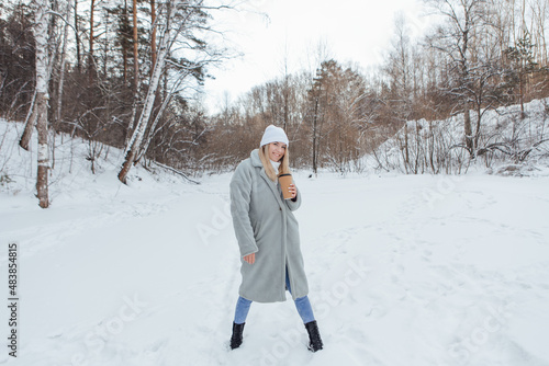 A beautiful young girl smiling and enjoying drinking coffee in a winter forest.