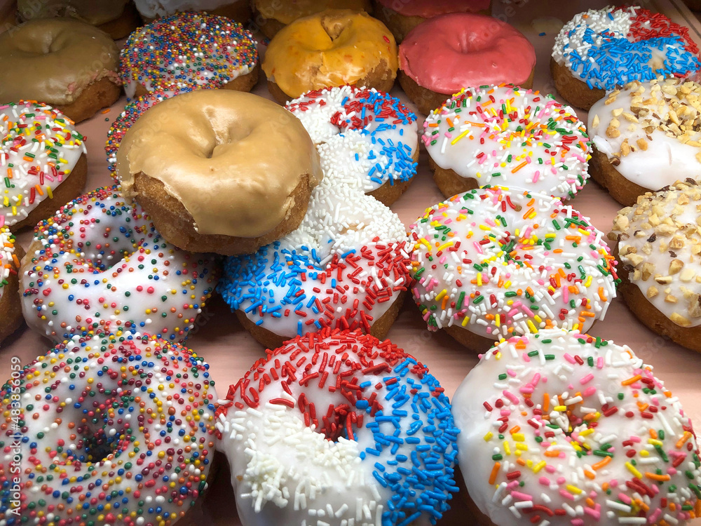 Vanilla frosted donuts with candy sprinkles on display for sale. High sugar fast food treat