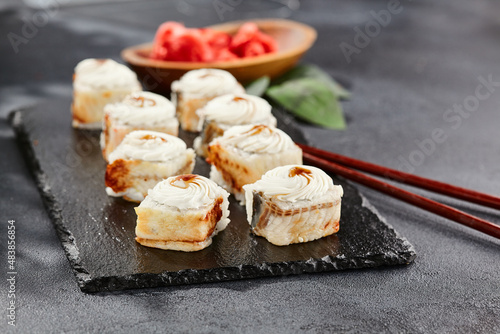 Maki sushi on dark slate. Unagi maki with eel. Sushi roll with eel fish, cream cheese and unagi sauce. Style concept japanese menu with black background, leaves and hard shadow.