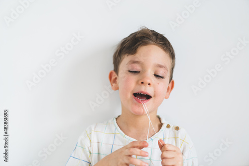 Cute boy pulling loose tooth using a dental floss. The boy's first milk tooth is loose. Toothache. Process of removing a baby tooth. Emotions of a child photo