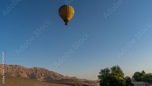 A bright yellow balloon is flying in the blue sky. A picturesque mountain range and green trees below. Copy space. Egypt. Luxor