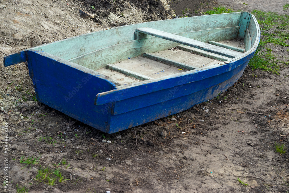 blue wooden boat is lying on the ground, on the shore, drying, pulled out blue wooden boat is lying on the ground, on the shore, drying, pulled out