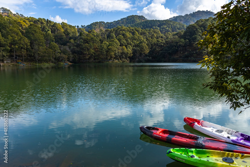 Colorful boats on the shore of a lake with the reflection of sky and hills 