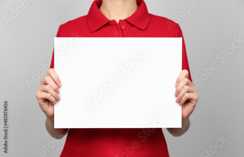 Woman hand holding blank paper label and mockup for design advertising on gray background.