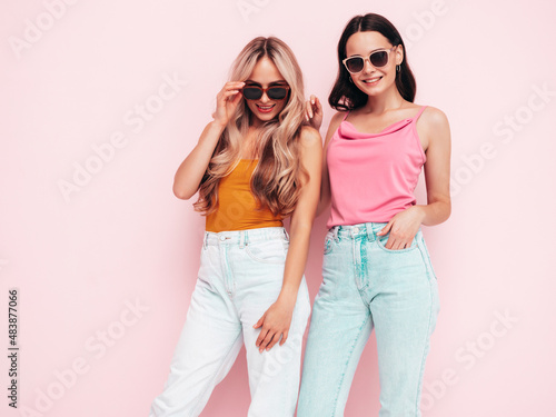 Two young beautiful smiling brunette hipster female in trendy summer clothes.  carefree women posing near pink wall. Positive models having fun. Cheerful and happy. In sunglasses © halayalex
