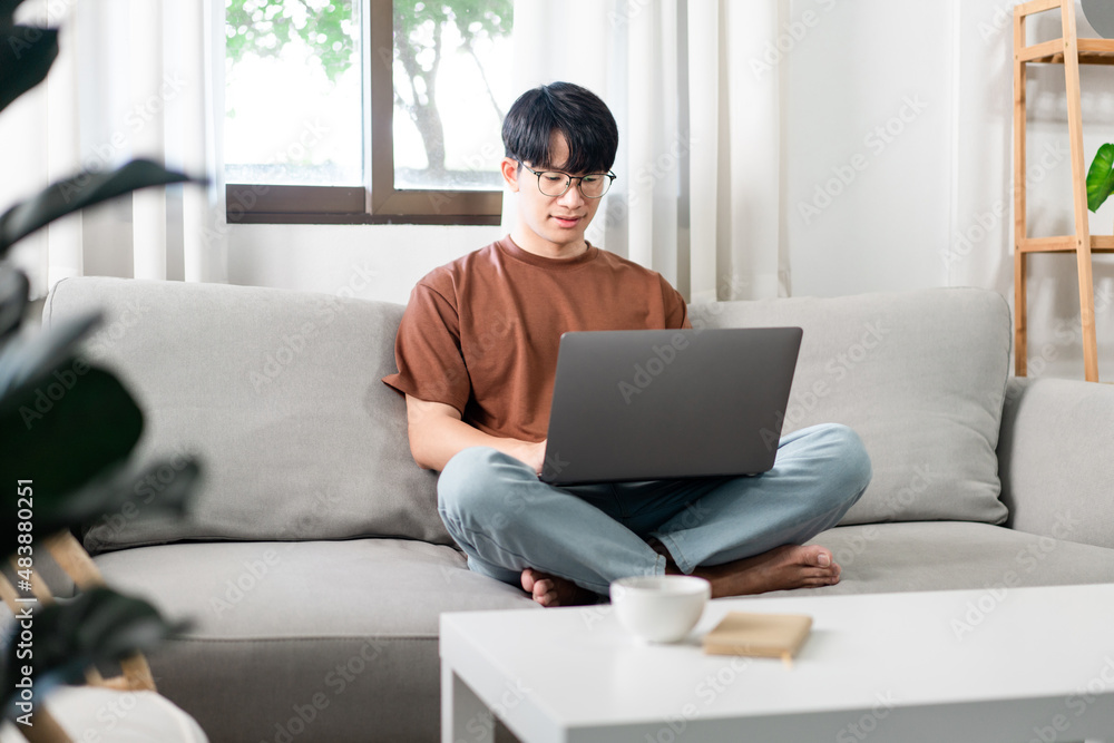 Technology Concept The male who is wearing casual clothes sitting on the sofa, resting his notebook on his lap and doing his work Technology Concept The male who is wearing casual clothes sitting on the sofa, resting his notebook on his lap and doing his work