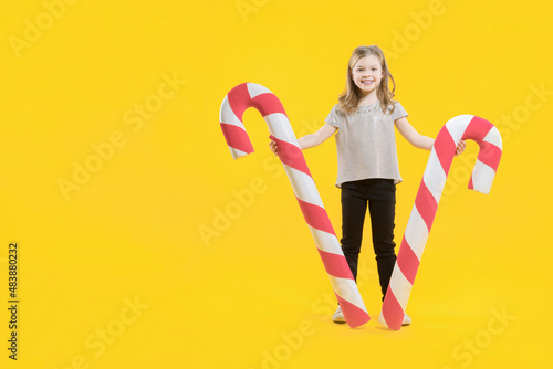 Happy preschooler with sweets in hands. Lollipop. A cute teenage girl holding two huge candies on a yellow background. Christmas sweets. Copy space. © watman
