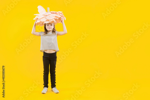 March 8. Women s day. The daughter is preparing a congratulation for her mother. Mothers day. Gift for mom. The girl holds a huge flower above her head on a yellow background. Copy space.