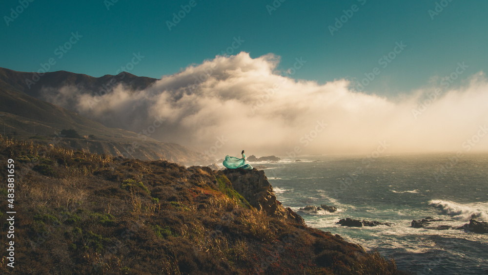 A girl looking out to the sea at a windy cliff in Big Sur