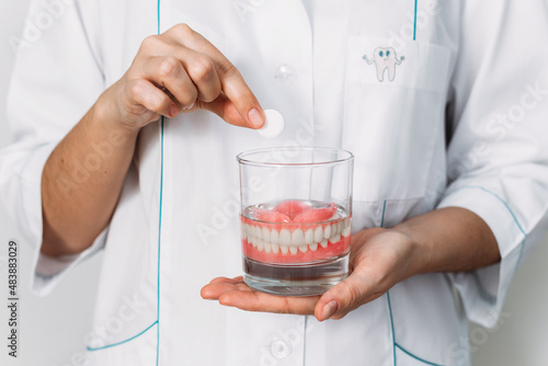 An orthopedic dentist shows how to take care of dentures, close-up. Dental implant care. A complete removable denture in the hands of a doctor. Oral hygiene. Copy space