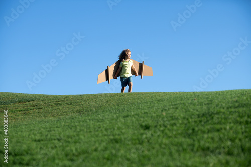 Freedom kids, boy playing to be airplane pilot, funny guy with cardboard wings as an airplane. Child pilot aviator with paper airplane dreams of traveling.
