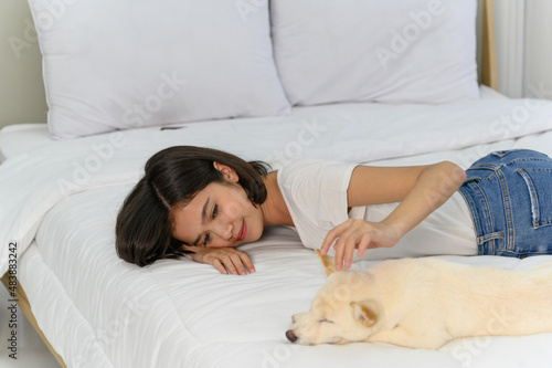 Young Asian woman lying with white Shiba Inu puppy sleeping on a white bed, Cheerful and nice couple with people and pet. Pet Lover concept