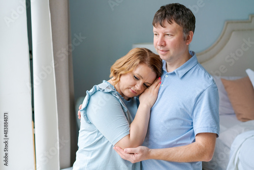 Dreamy couple family connection cuddling looking into distance through window. Loving gentle homeowners, man and woman, visualize a shared future and enjoy a new beginning indoors together. © Екатерина Переславце