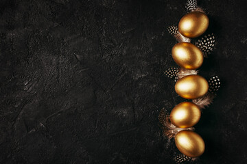 Happy easter concept flat lay with gold eggs and feather on black background