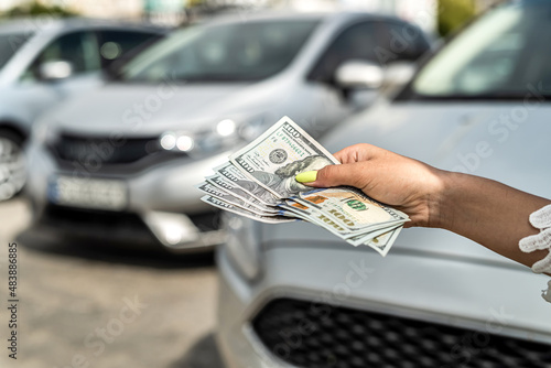 male hand holding a lot of dollars against gray car in the back