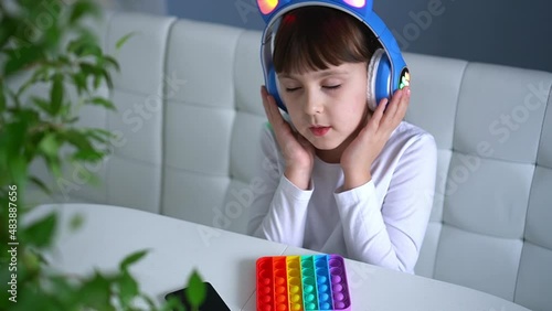 Baby girl playing with rainbow pop it fidget and listening music with headphones