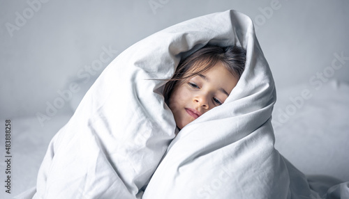 Sleepy little girl wrapped in a white blanket.