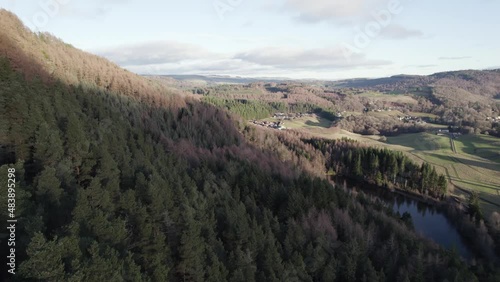 Aerial drone footage panning away from a cliff and forest on a mountain at Polney Crag (Craig a Barns) near Dunkeld Scotland in sunlight to reveal a beautiful landscape of trees, a field and lochs photo