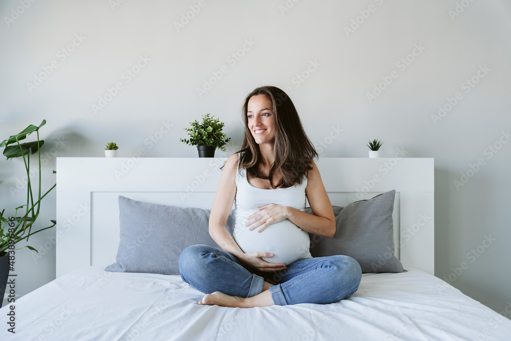 Smiling pregnant woman sitting cross-legged on bed at home Smiling pregnant woman sitting cross-legged on bed at home