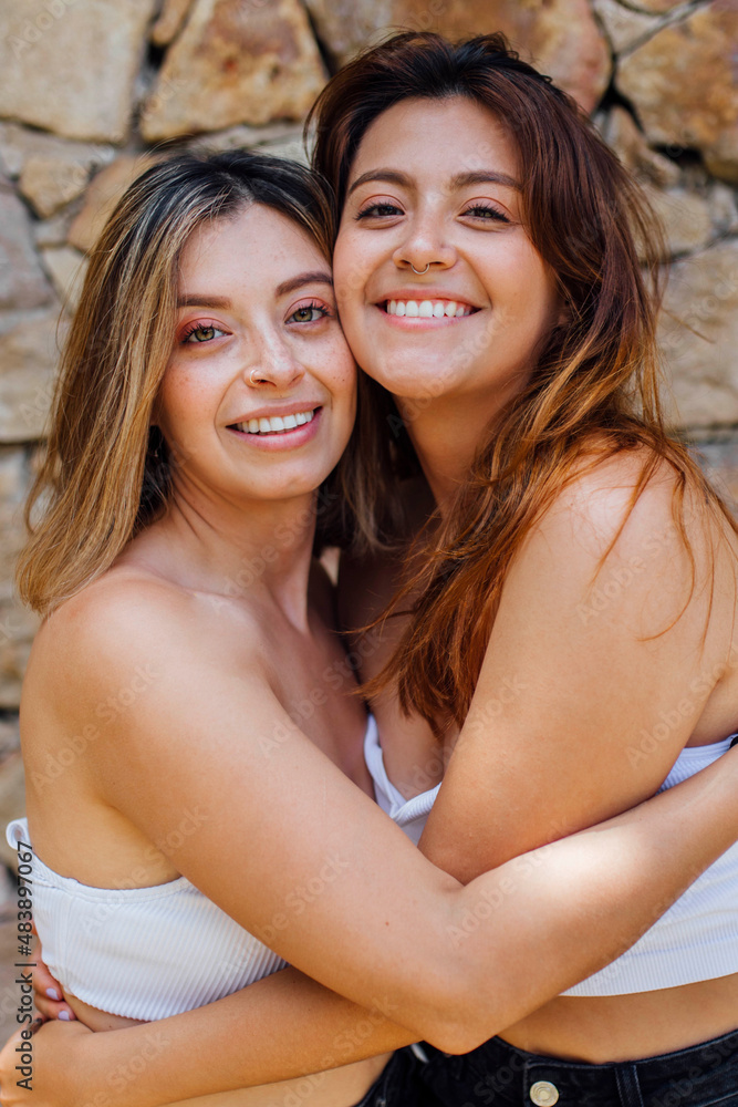 Smiling young women embracing in front of wall Smiling young women embracing in front of wall