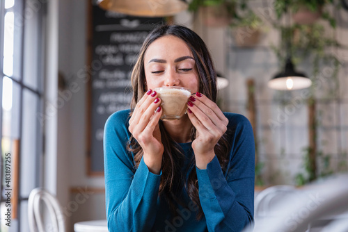 Happy woman drinking cappuccino in coffee shop photo