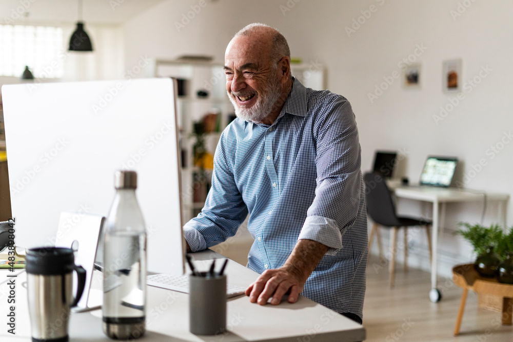 Cheerful senior businessman using computer at desk Cheerful senior businessman using computer at desk
