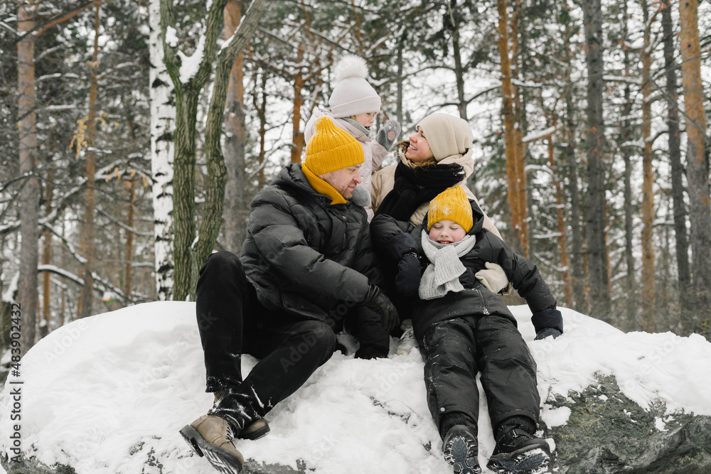 Man and woman sitting with daughter and son on snow in winter forest Man and woman sitting with daughter and son on snow in winter forest