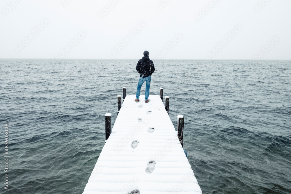 Hiker admiring lake standing on snow covered jetty in winter, Walchensee, Bavaria, Germany Hiker admiring lake standing on snow covered jetty in winter, Walchensee, Bavaria, Germany
