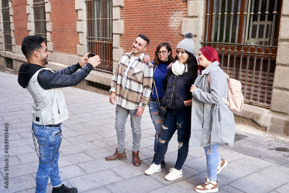 Obraz premium Latino man taking a picture with his smart phone of his group of friends on a city street. 