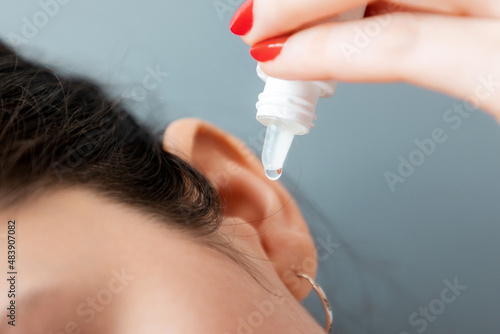 A woman drips medicine into her ear. Close-up. Gray background. The concept of otitis, hearing loss and hearing problems