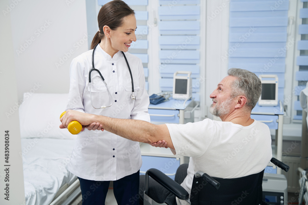 Obraz premium Male patient lifting hand weight assisted by friendly physiologist