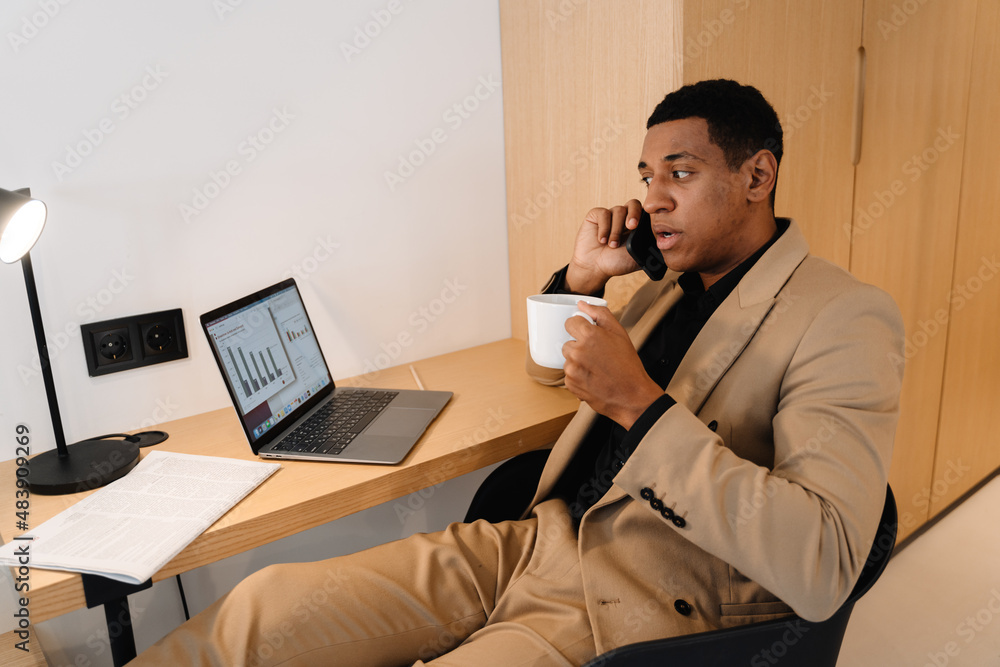 Black man talking on cellphone and drinking coffee while working in hotel Black man talking on cellphone and drinking coffee while working in hotel