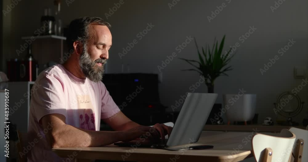 Side view of focused Hispanic middle-aged man with beard sitting at table and typing on laptop while doing remote work Side view of focused Hispanic middle-aged man with beard sitting at table and typing on laptop while doing remote work