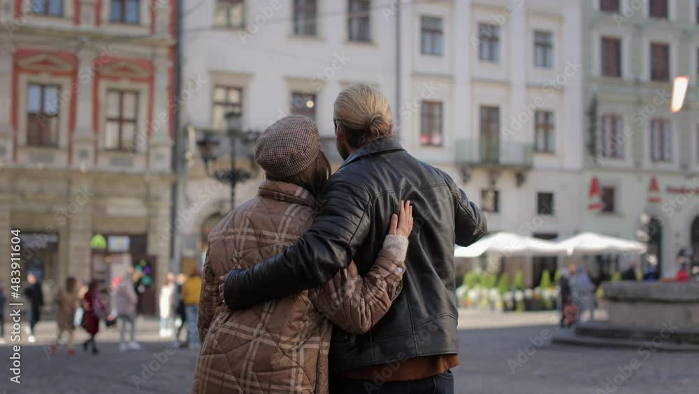 Back view of happy caucasian couple in stylish casual wear embracing and walking on street. Male and female tourist enjoying sightseeing of new city. Back view of happy caucasian couple in stylish casual wear embracing and walking on street. Male and female tourist enjoying sightseeing of new city.